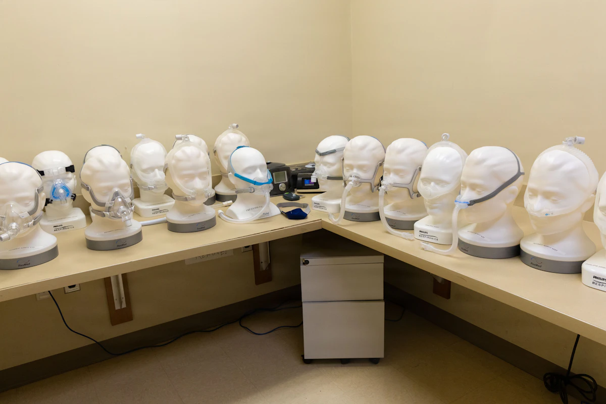 Verschiedene CPAP-Maskentypen auf Übungsköpfen in einer Praxis, Nasenmasken und Vollgesichtsmasken im Vergleich