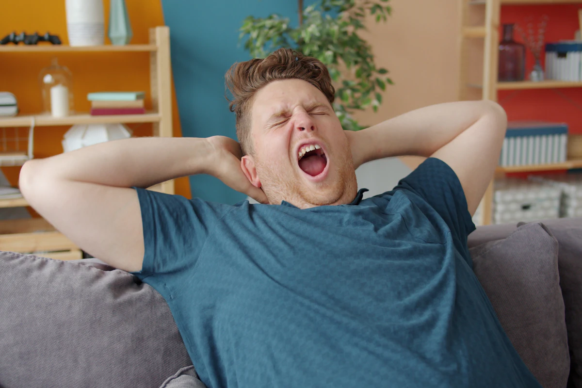 Erschöpfter Mann gähnt morgens auf dem Sofa, sichtlich übermüdet