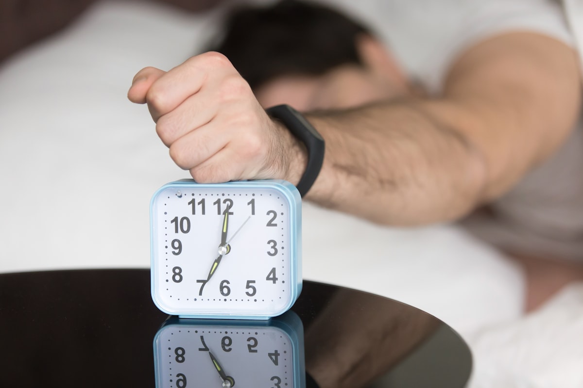 Mann greift verschlafen nach dem Wecker am Bett